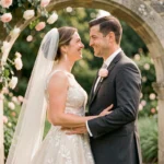 Couple de mariés se regardant tendrement lors d'une cérémonie de mariage en jardin français avec arches de roses